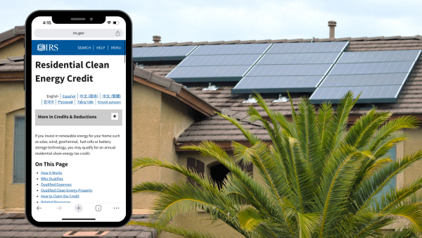 Phone with Residential Clean Energy Credit information from the IRS on it in front of home with rooftop solar